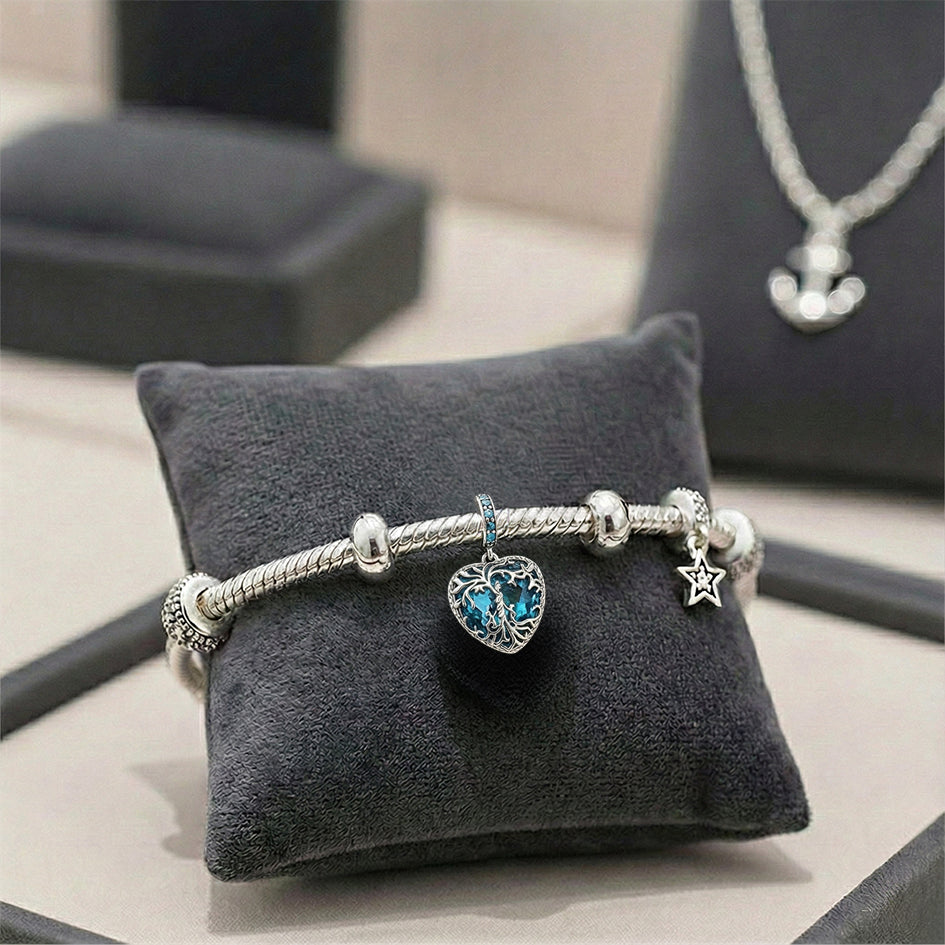 Silver bracelet with heart charm and star charm on a gray jewelry pillow.